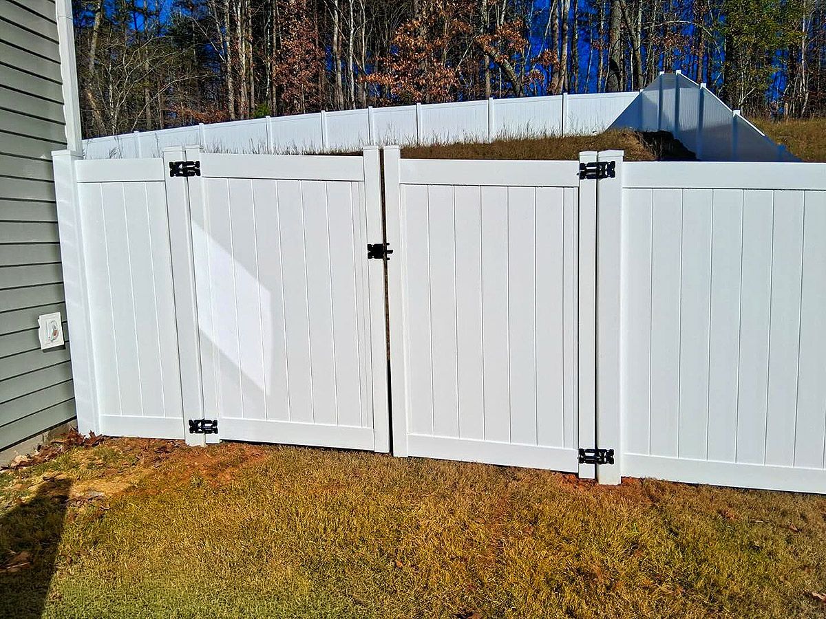 White vinyl fence and gate in a backyard with grass and a house in the background.