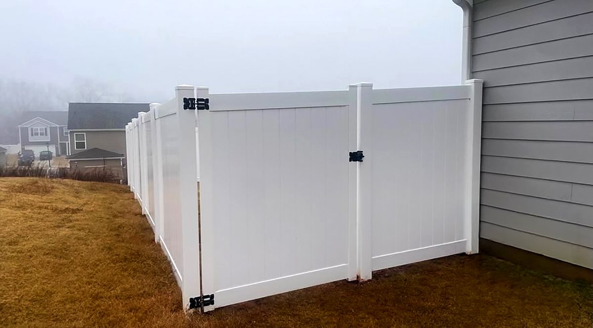 White vinyl fence gate beside gray house on a foggy suburban lawn