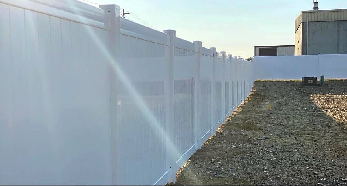 White fence along a gravel path in bright sunlight, with a sunbeam across the scene.