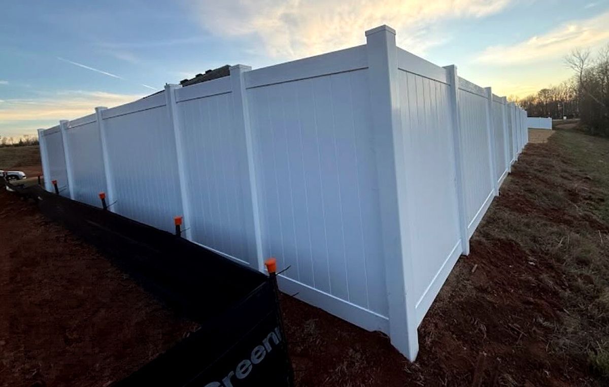 White vinyl fence panels forming an enclosed yard on a dirt lot at sunset