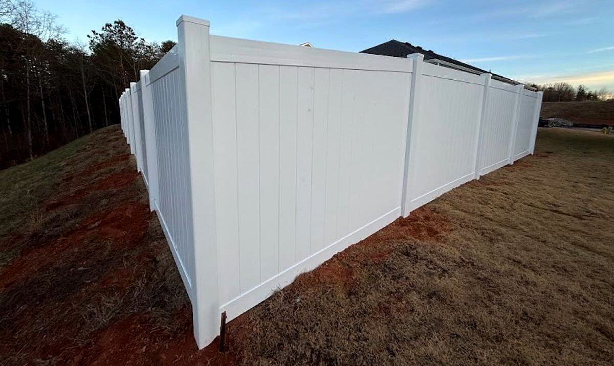 White vinyl privacy fence along a sloped yard at dusk