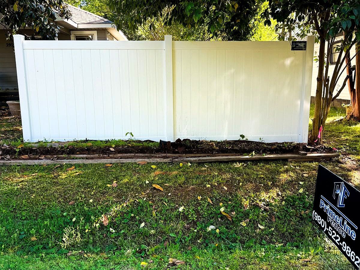 White vinyl fence in a grassy yard with trees and a small sign at the lower right.