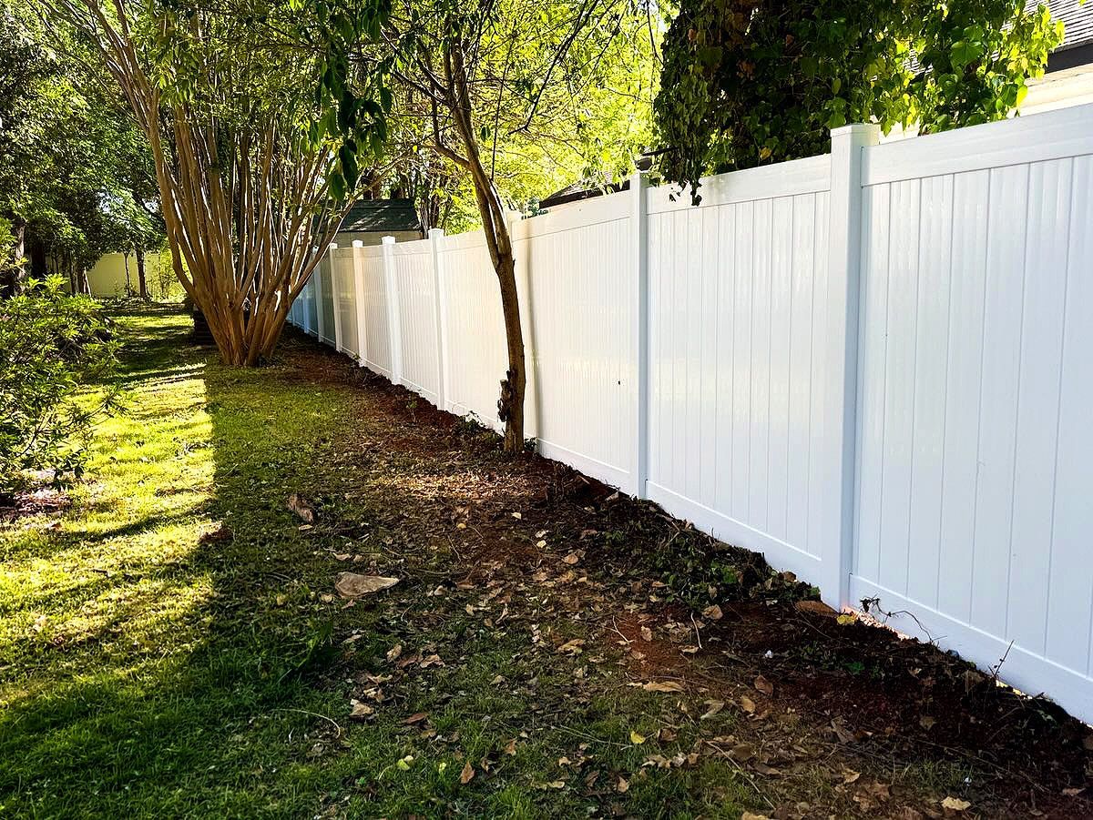 White vinyl fence beside a grassy yard with trees and a narrow dirt path