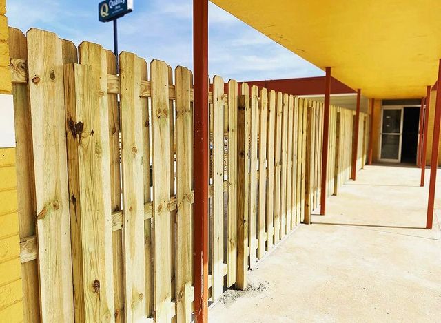 Wooden fence lining a sunny outdoor walkway beside a yellow building
