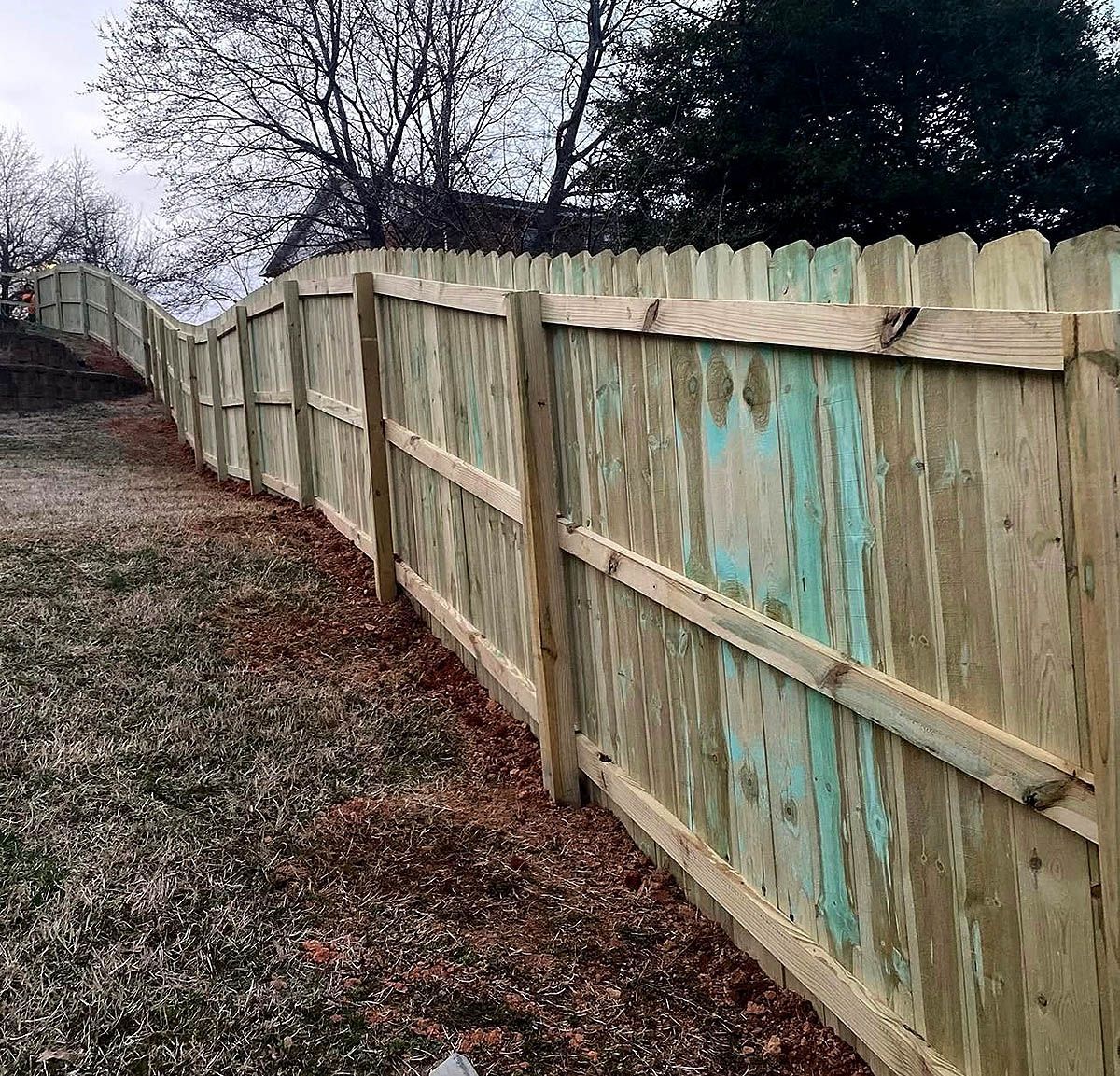 Weathered wooden fence lining a leafless yard on an overcast day