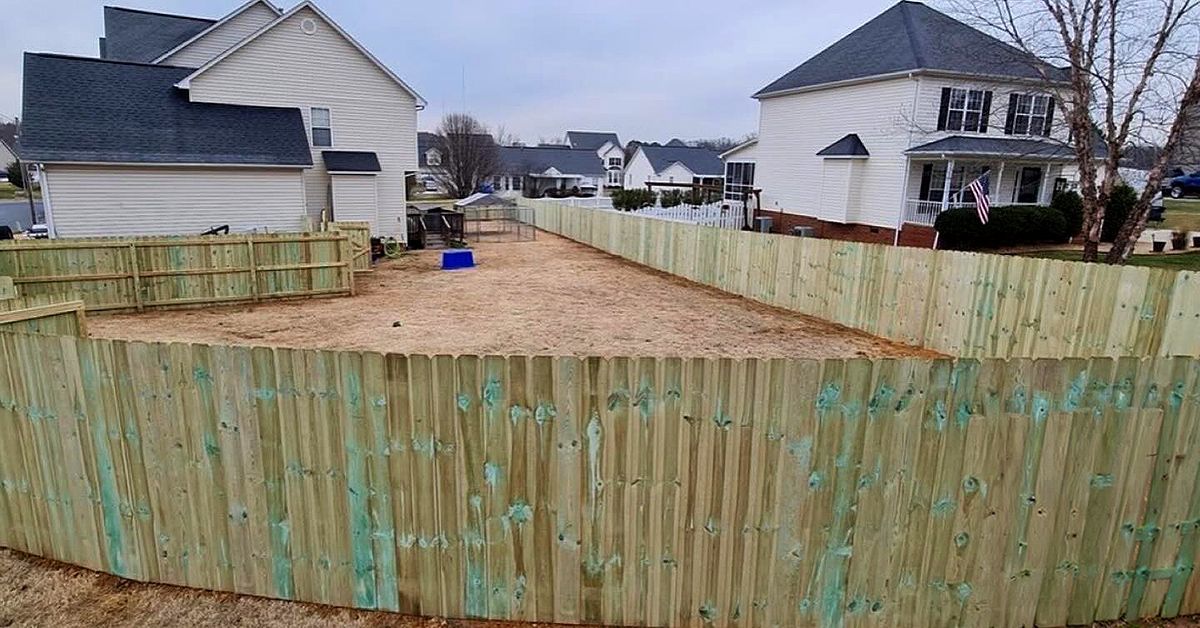Wooden-fenced backyard with a small blue object, surrounded by houses on an overcast day