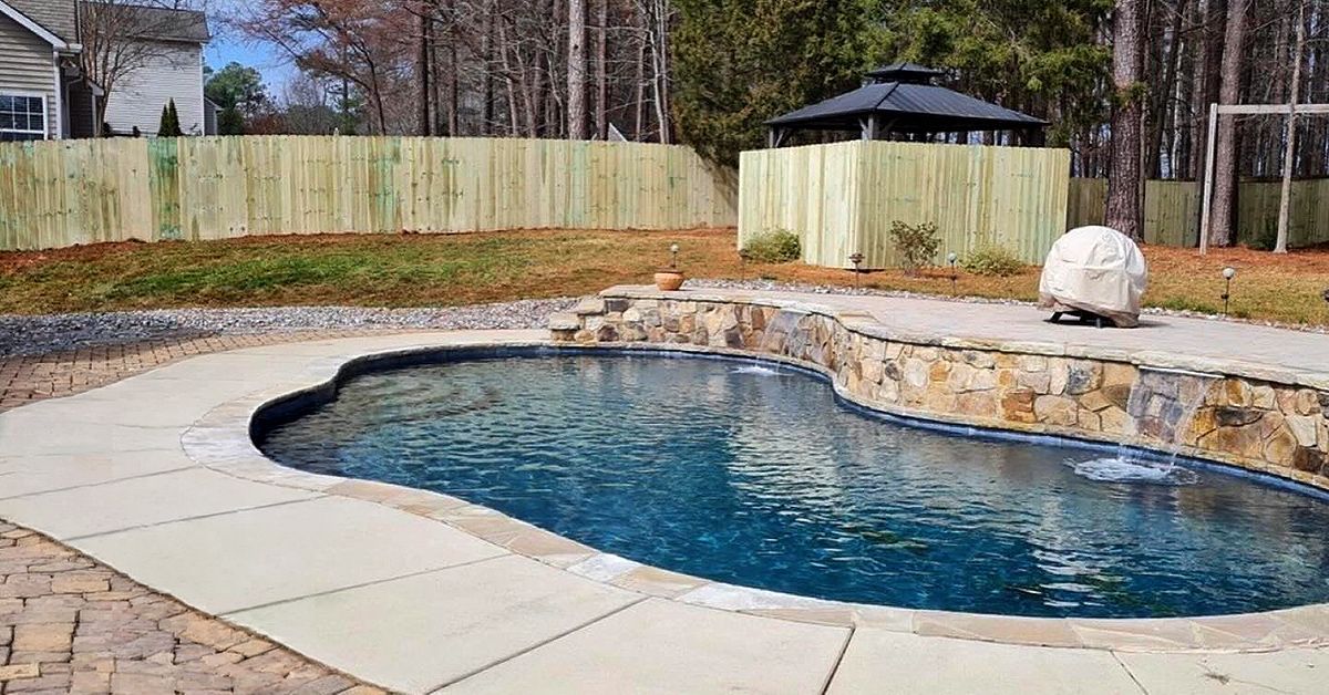 Backyard swimming pool with stone coping, concrete patio, and fenced yard