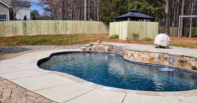Backyard swimming pool with stone coping, concrete patio, and fenced yard