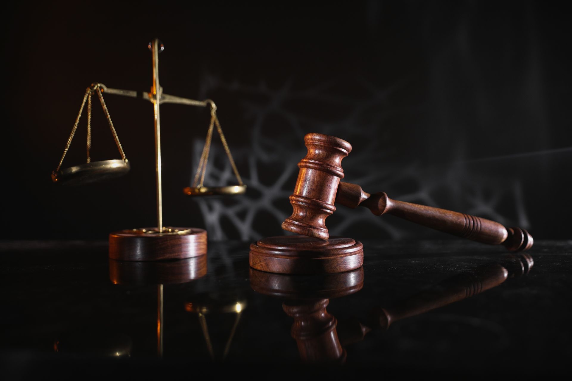 Scales of justice and a gavel on a reflective surface, set against a dark background.
