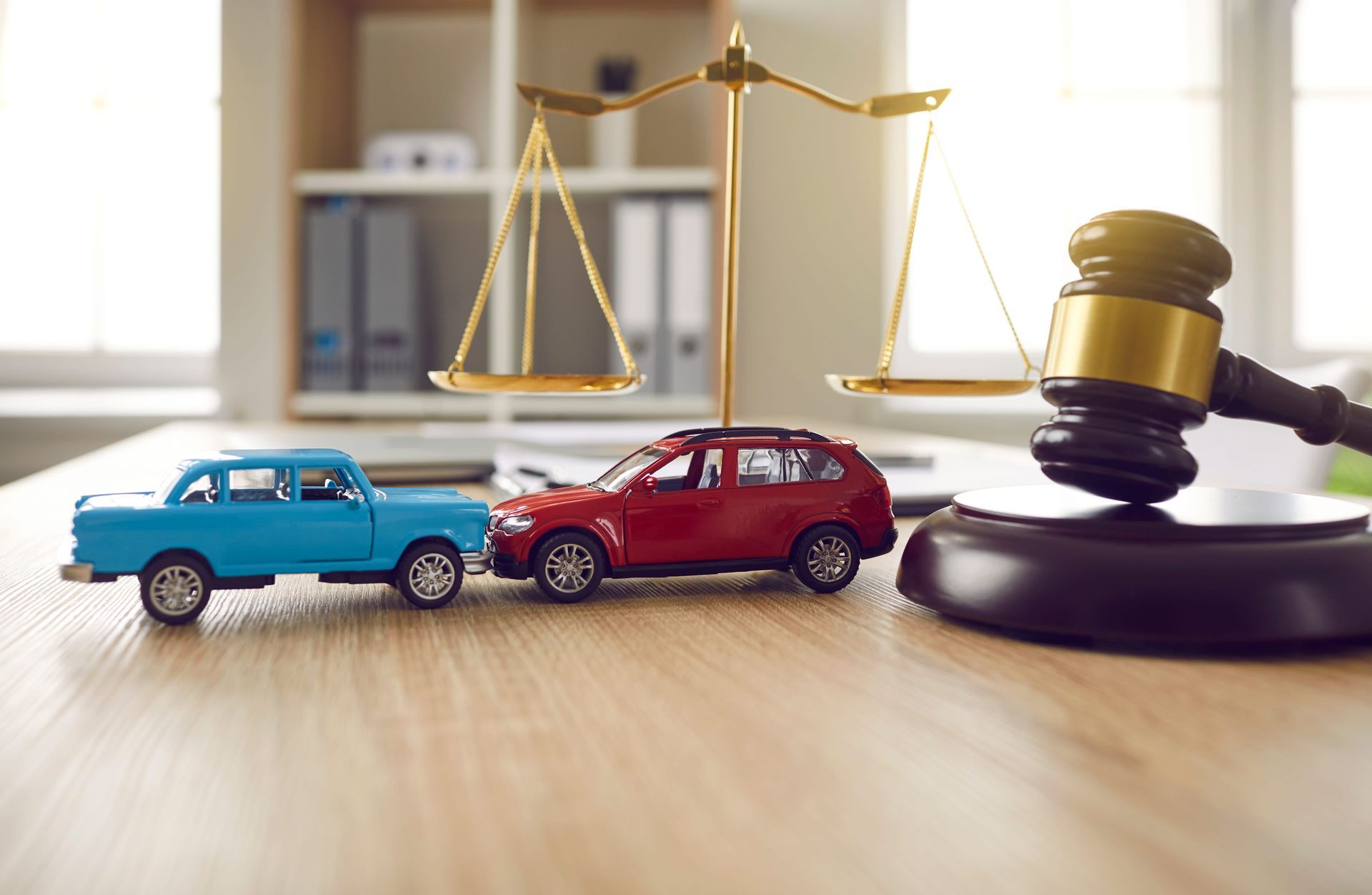 Toy cars and a gavel beside scales of justice on a desk, suggesting a legal accident claim