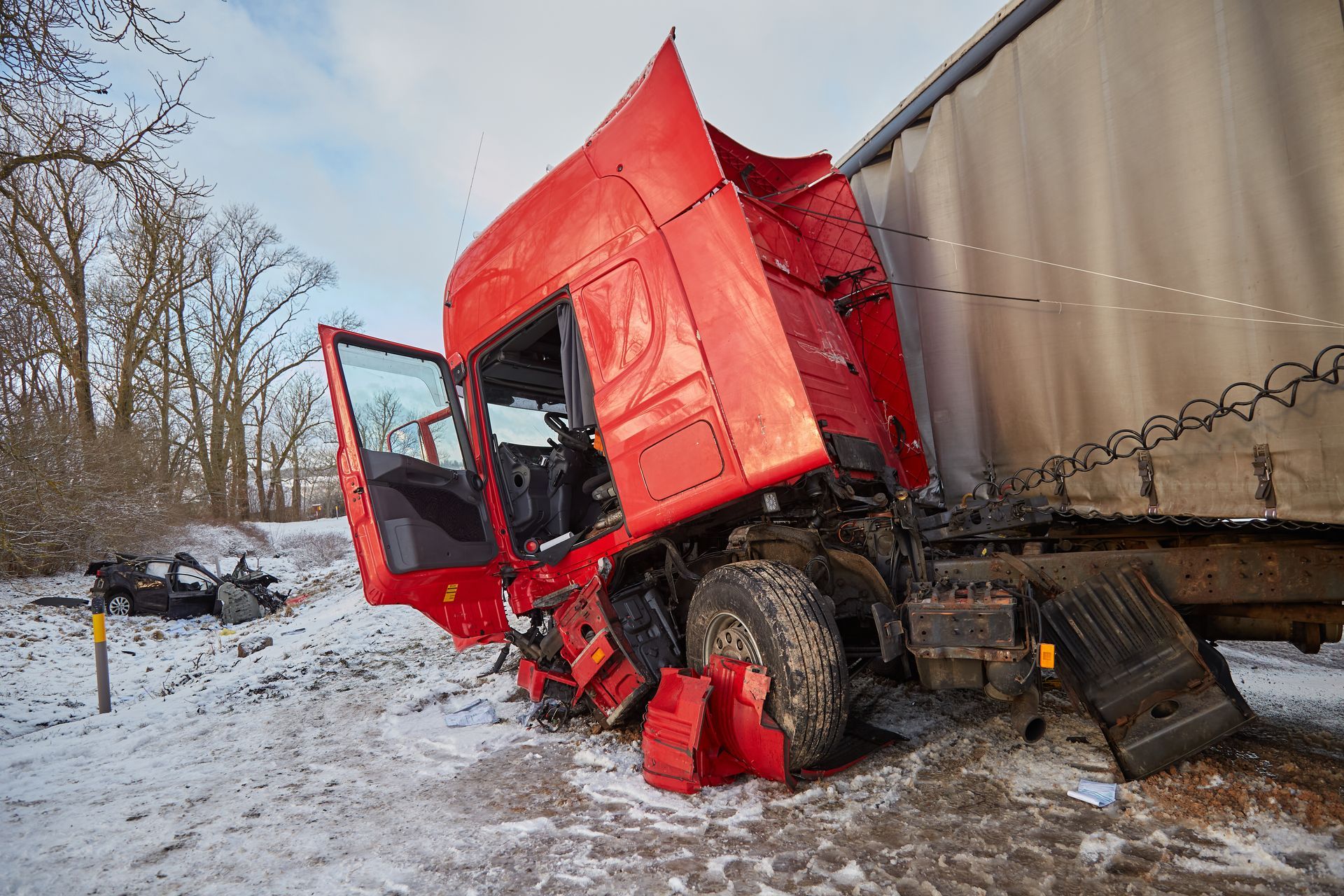 Red semi-truck cab damaged and tilted, colliding with trailer on snowy roadside.