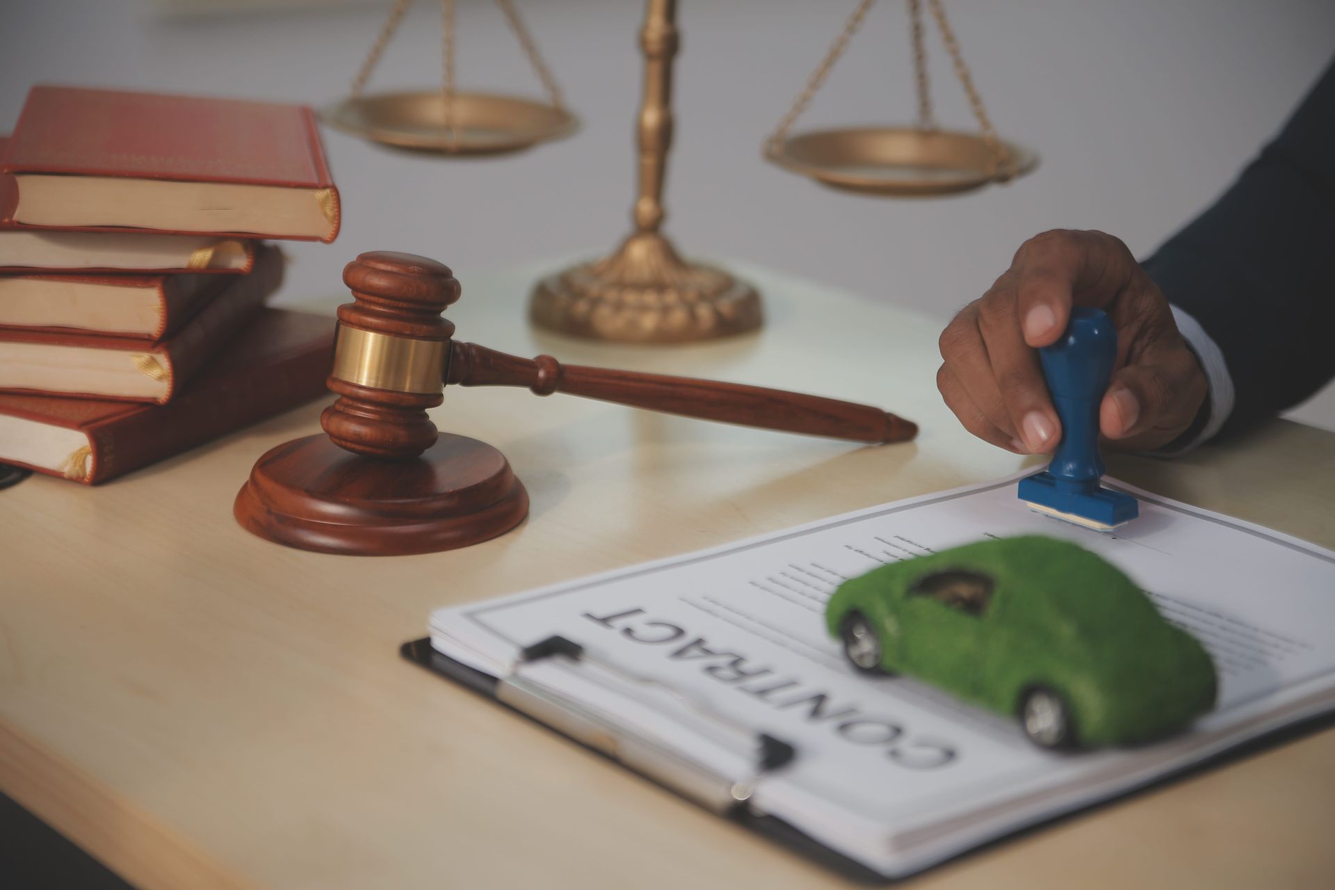 Legal contract being stamped with a green toy car, gavel, and balance scales on a desk