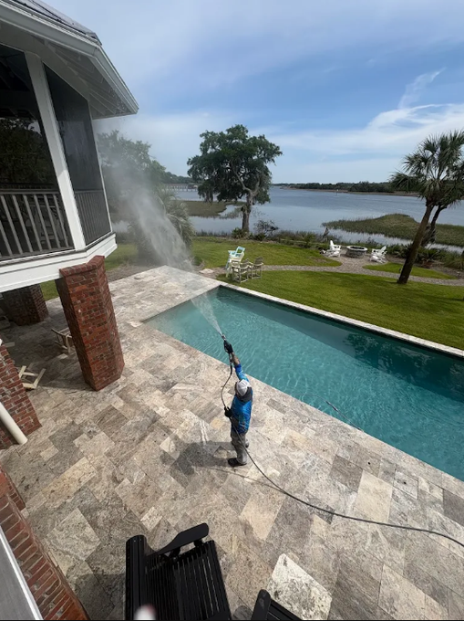 Person pressure-washing a patio beside a pool overlooking a lake