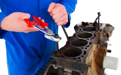 Mechanic in blue jumpsuit using pliers and a wrench on an engine block, white background.