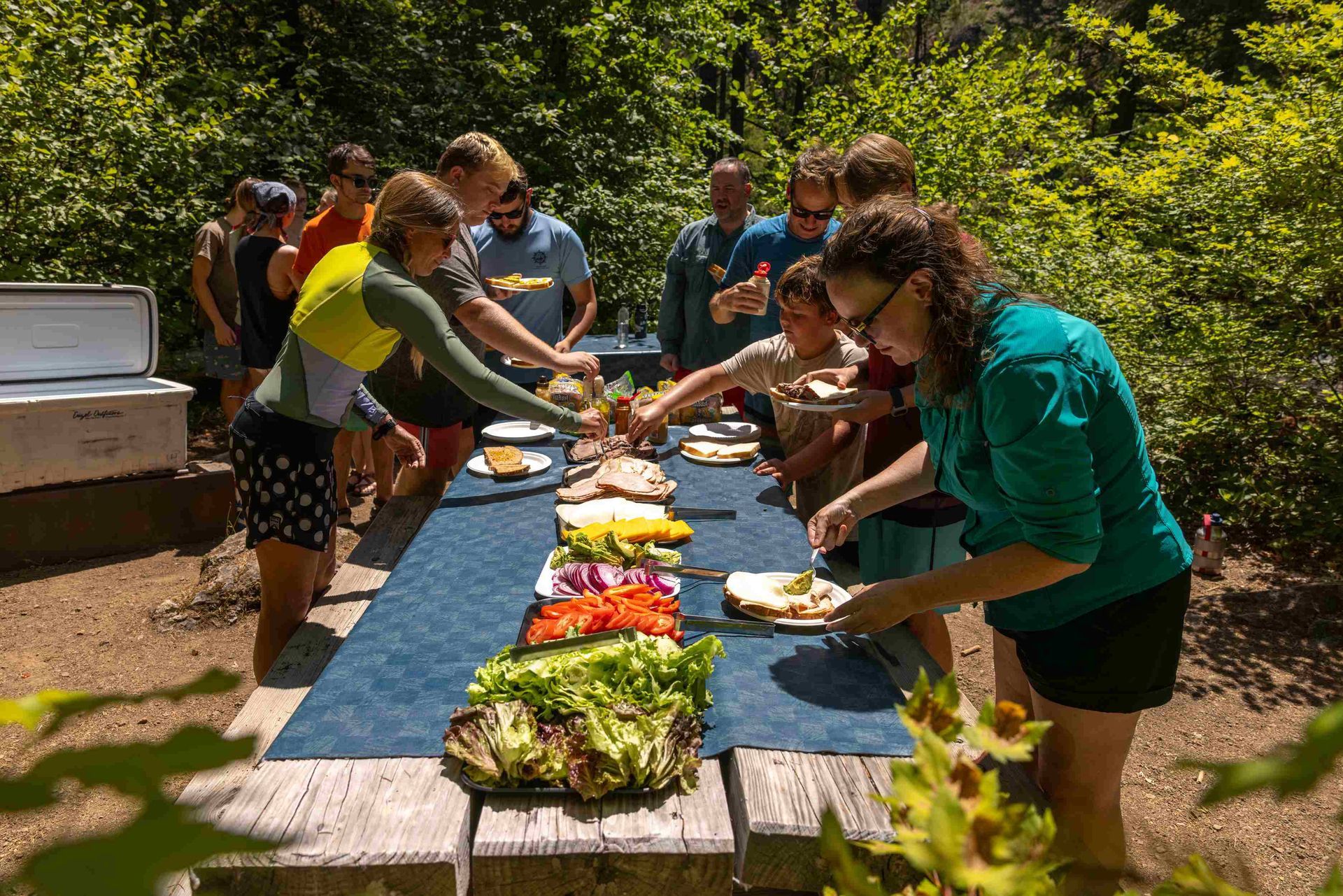 A group of people are standing around a picnic table eating food.