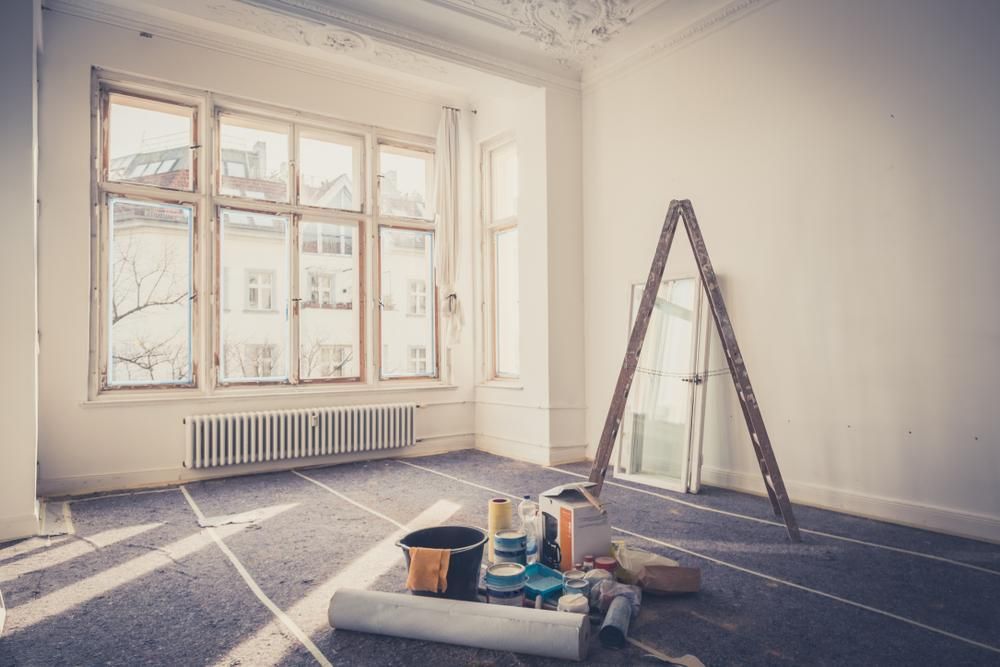 An empty room with a ladder and paint buckets on the floor.