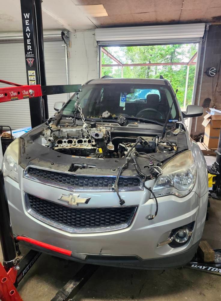 Silver Chevrolet SUV with front end disassembled in a repair shop lift bay