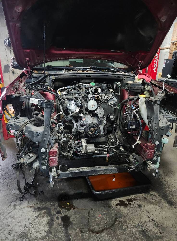 Car engine bay with front body removed, hood open, and orange drain pan underneath in a workshop