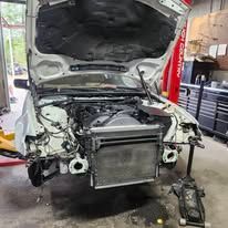 Damaged white car with open hood in an auto repair shop, front end removed and exposed radiator visible