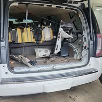 Cargo van interior with exposed equipment and damaged panels, rear doors open in a garage-like setting