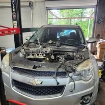 Damaged silver car with engine exposed in a garage or repair shop