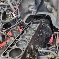 Car engine block with cylinder bores exposed, surrounded by hoses and wires in a workshop.