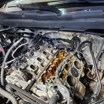 Open car engine bay with exposed cylinder heads and hoses during repair