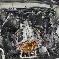 Disassembled car engine in a cluttered garage, with exposed cylinder block and parts around it