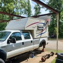 White pickup truck under a carport, with one wheel removed and axle parts on the ground.