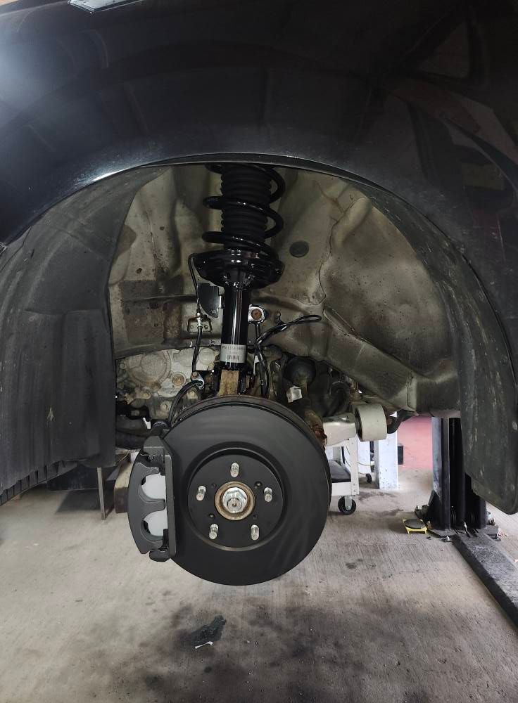 Front wheel and suspension assembly inside a car’s wheel well during repair.