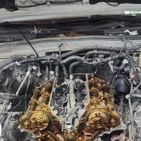 Engine bay with a disassembled engine showing exposed camshafts and oily rust-colored components.