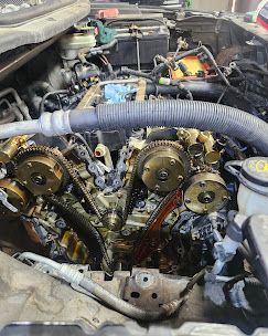 Car engine with timing cover removed, exposing cam gears and chain in the engine bay