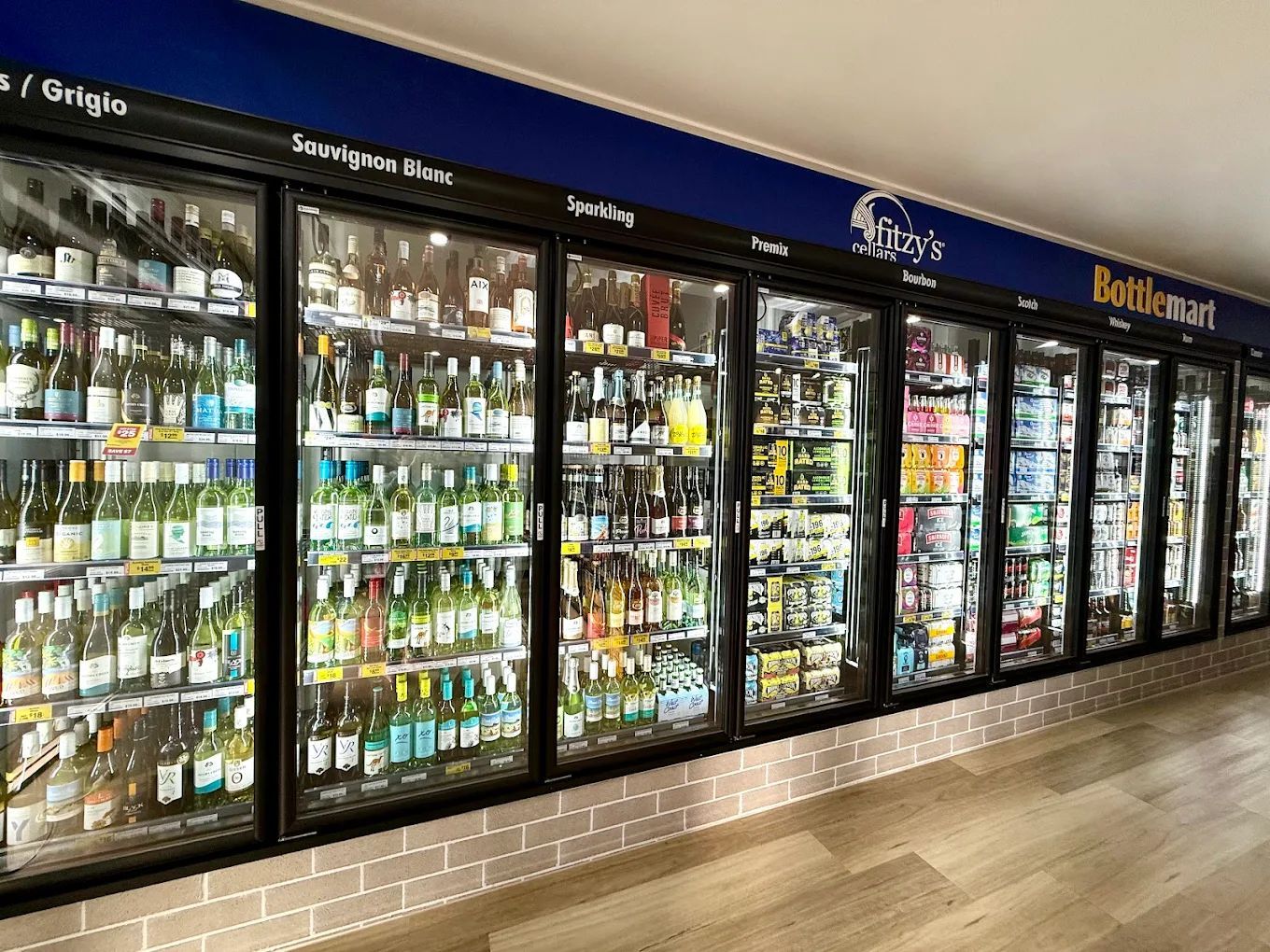 Long refrigerated beverage cases in a grocery store, filled with drinks and lit by bright cooler lights.