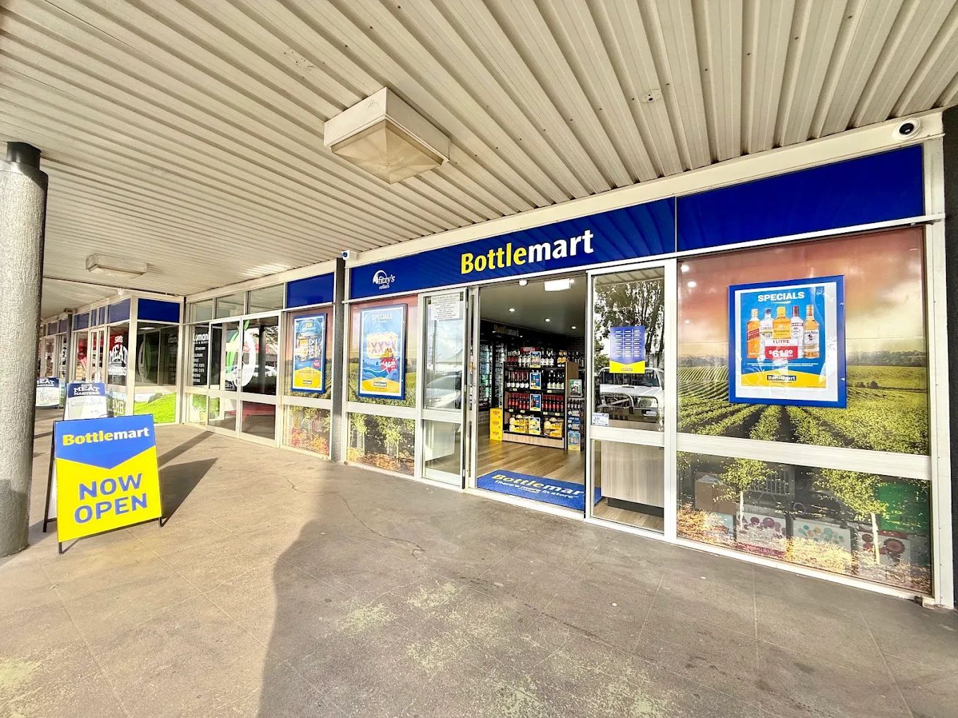 Exterior of a Battlemart convenience store with glass doors and bright blue signage, seen under a covered walkway.