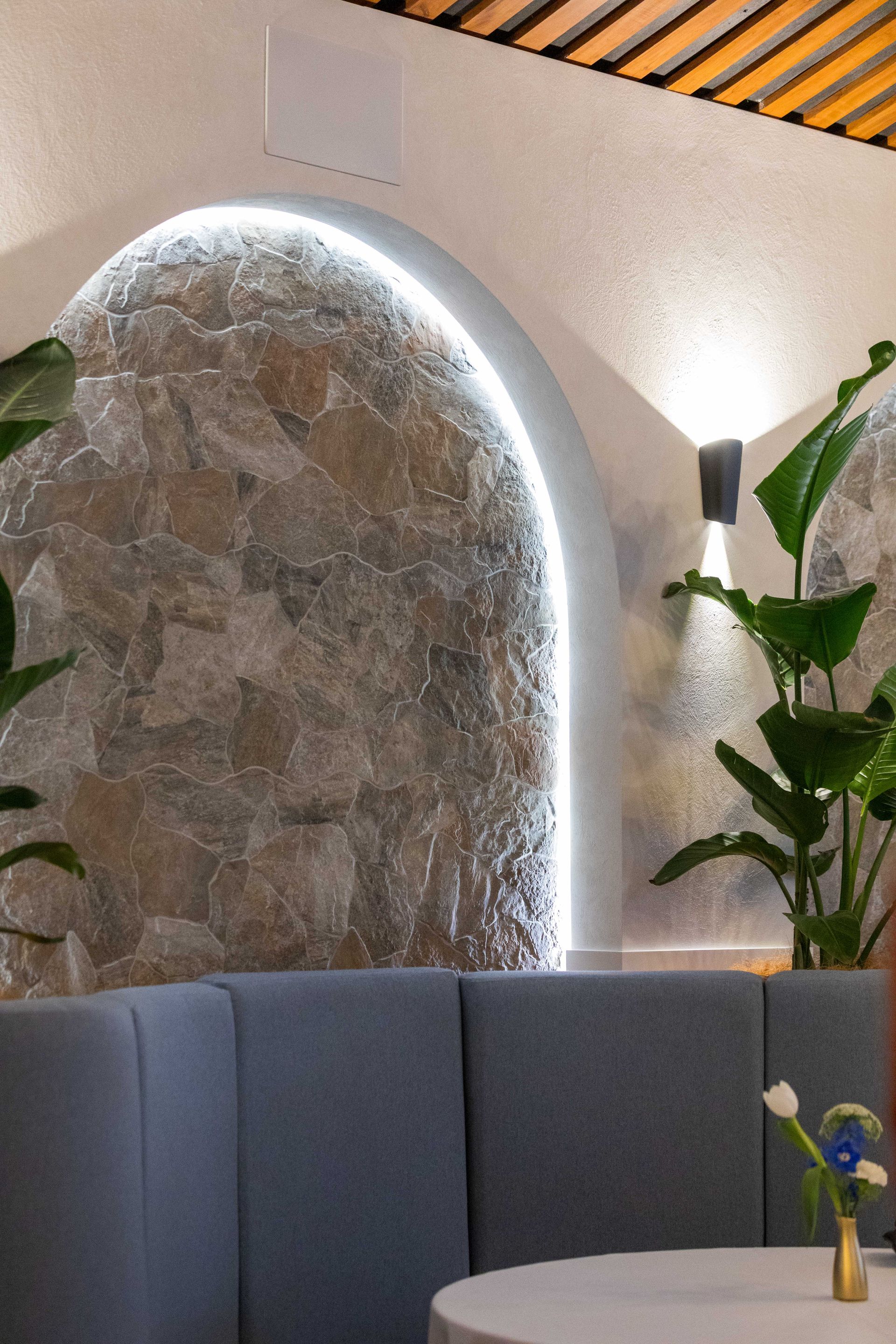 Modern lobby with a curved stone wall, blue seating, warm lighting, and a potted plant