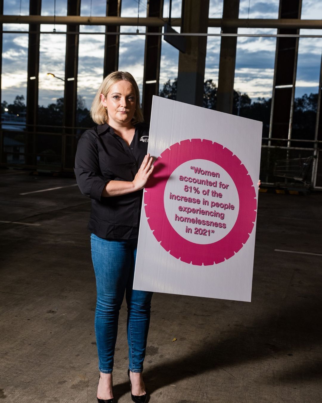 A woman in a black shirt is holding a sign that says women encompassed