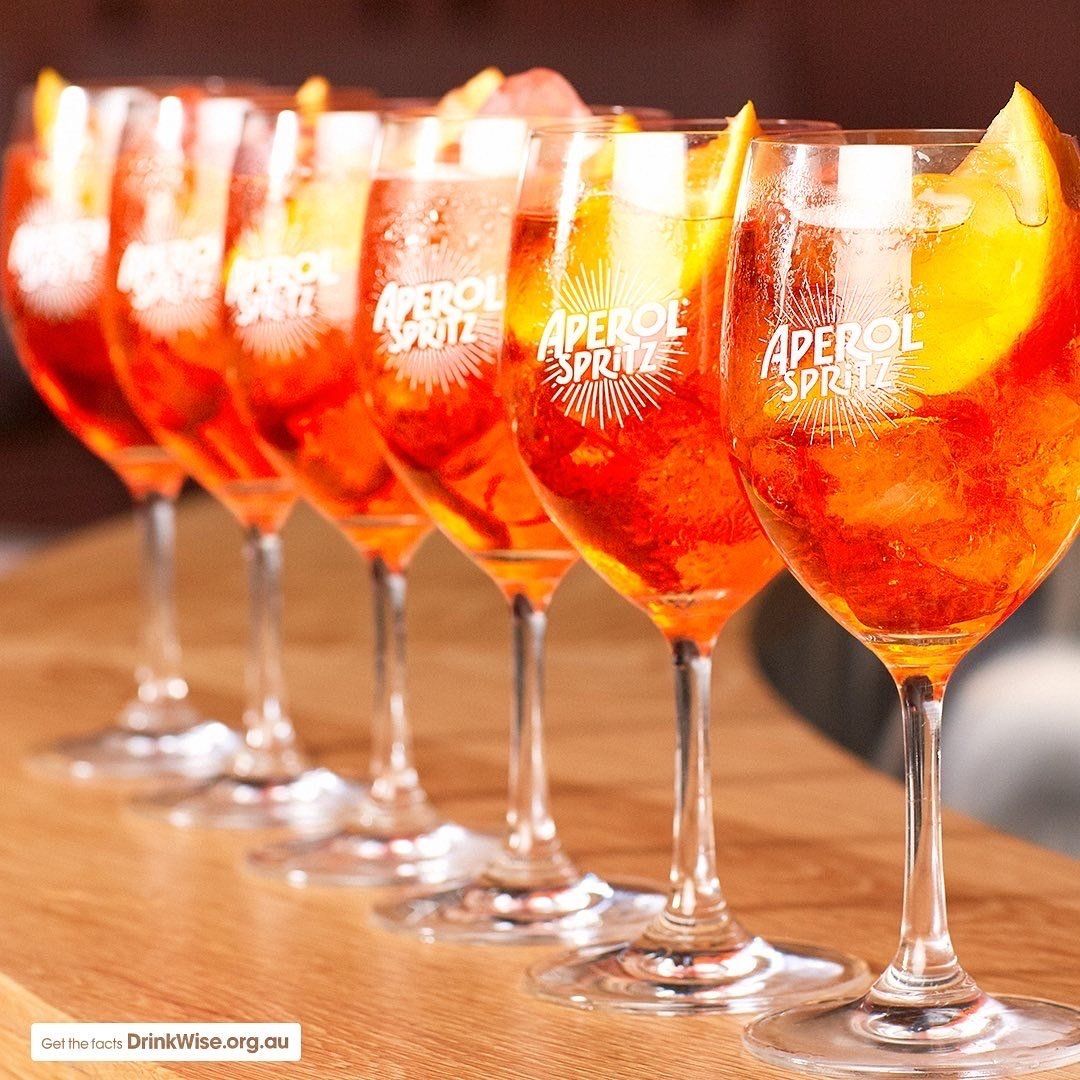 A row of aperol spritz glasses on a wooden table