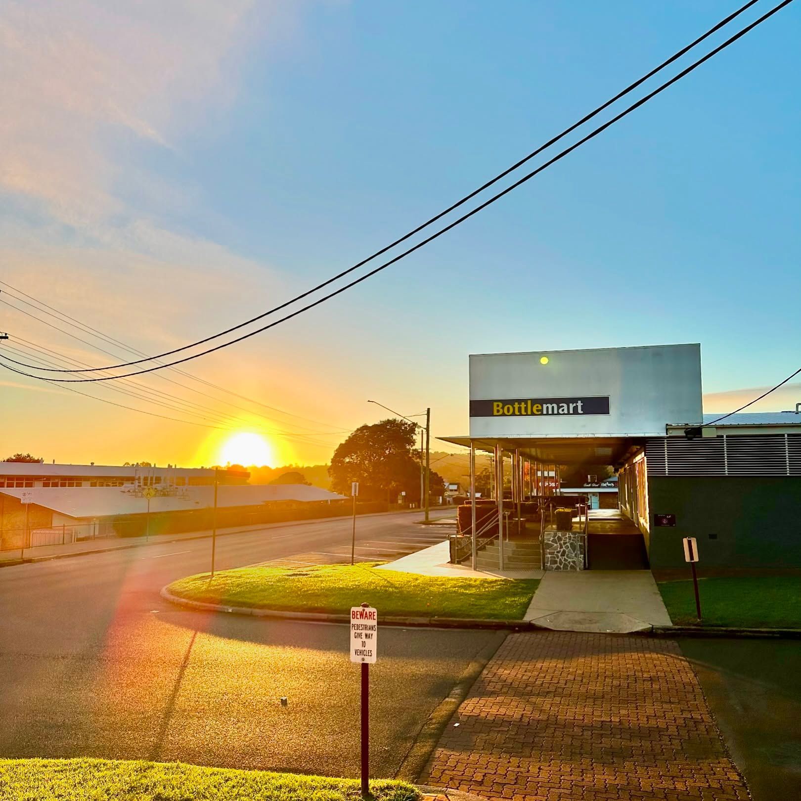 Sunrise over Bottle-O Mart, with street and power lines.