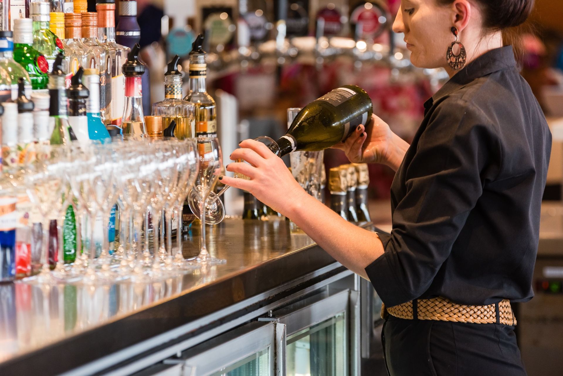 Bartender pouring a cocktail behind a bar lined with bottles and glasses