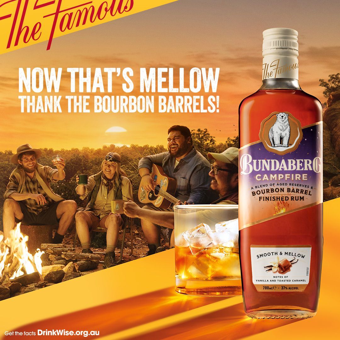 A bottle of bundaberg campfire rum next to a group of men sitting around a campfire