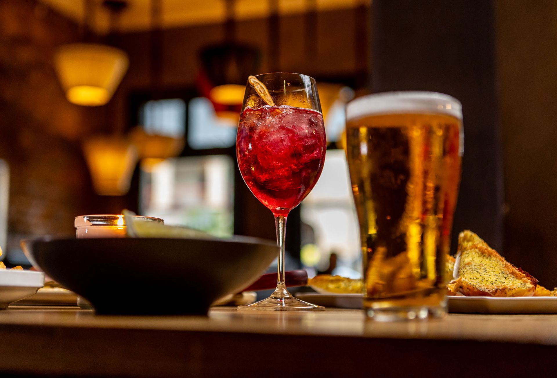 A table with a red cocktail, beer, and snacks.