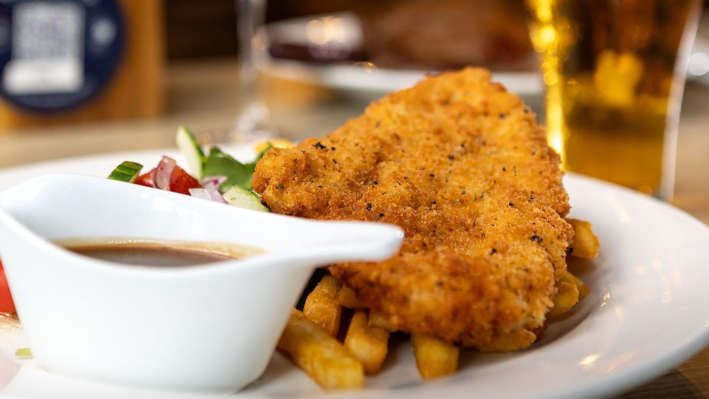 Plate with fried chicken, fries, gravy, and salad, with a beer in the background.