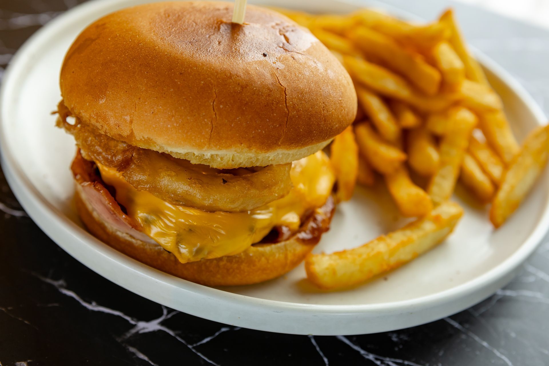 Burger with onion rings and fries on a white plate.
