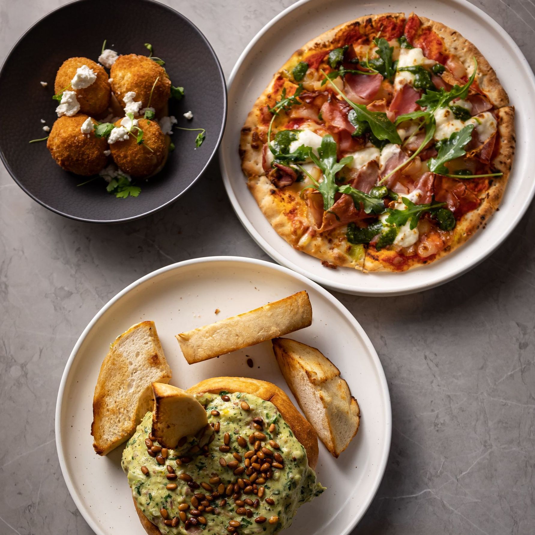 Three plates of food on a table including a pizza