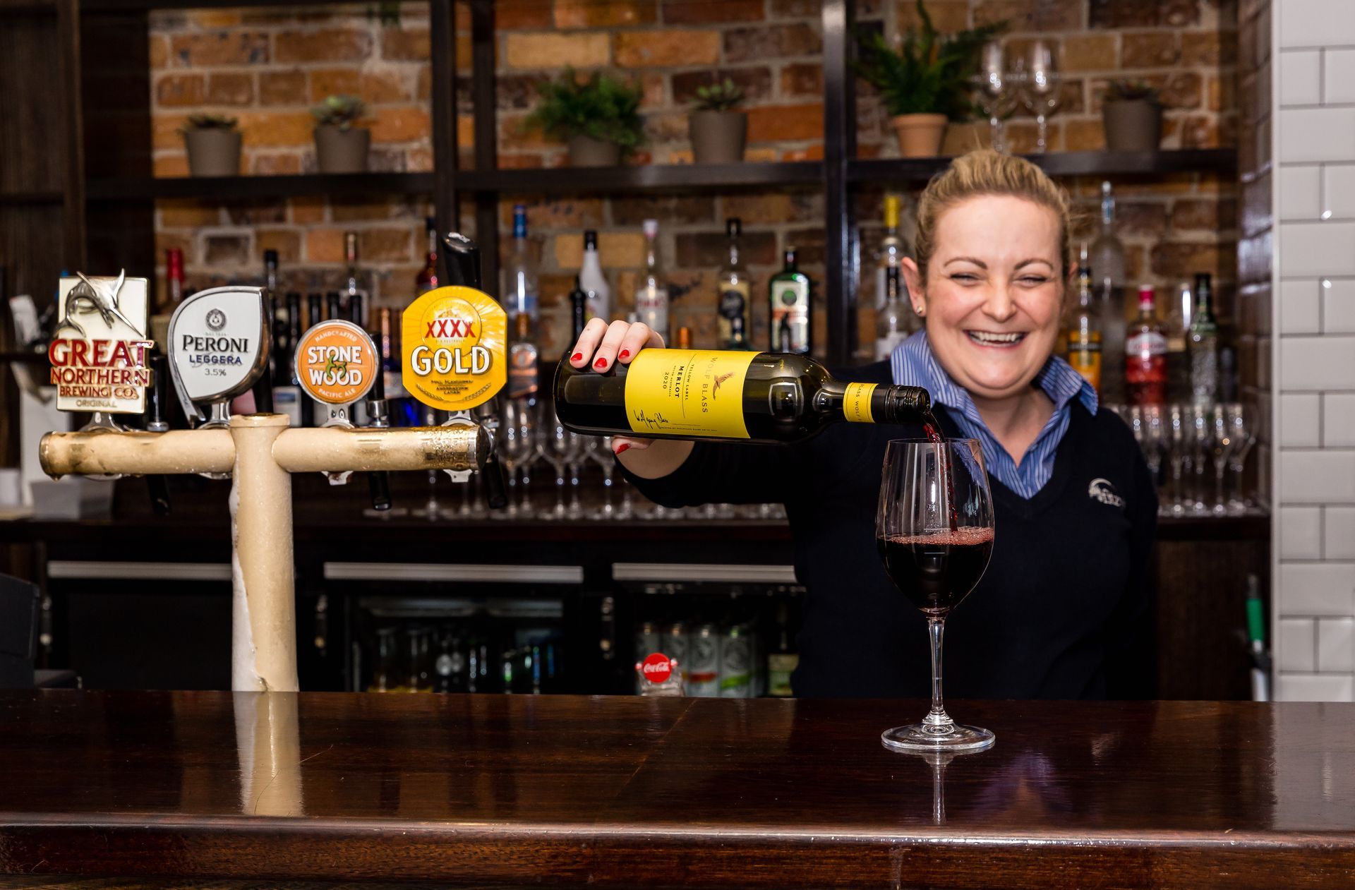 A woman is pouring wine into a glass at a bar.