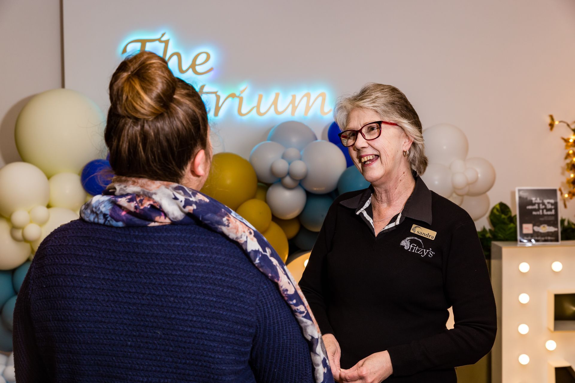 Two women are talking to each other in front of balloons.