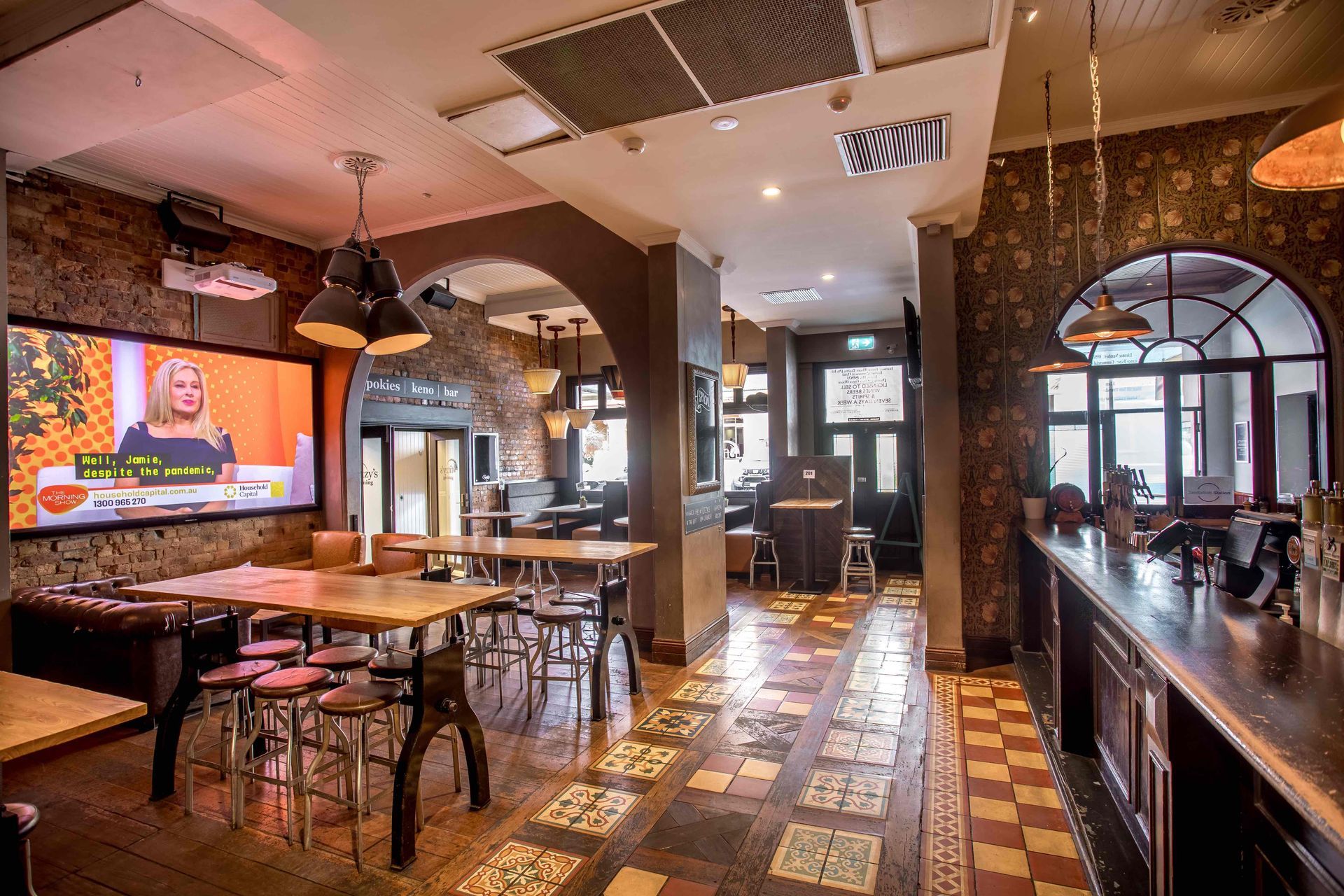A restaurant with tables and chairs and a large screen on the wall.