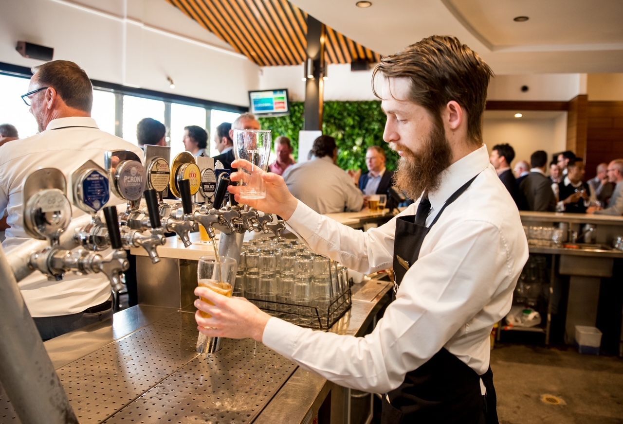 A man with a beard is pouring beer into a glass at a bar.