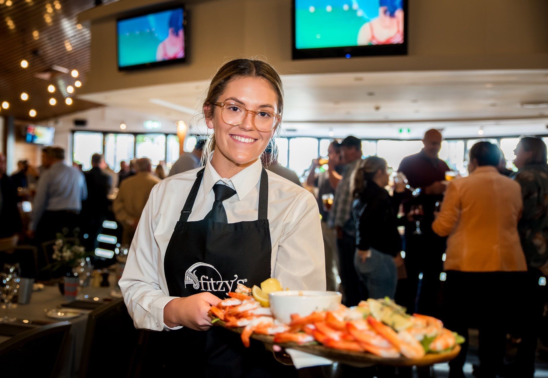 A waitress is holding a tray of shrimp in a restaurant.