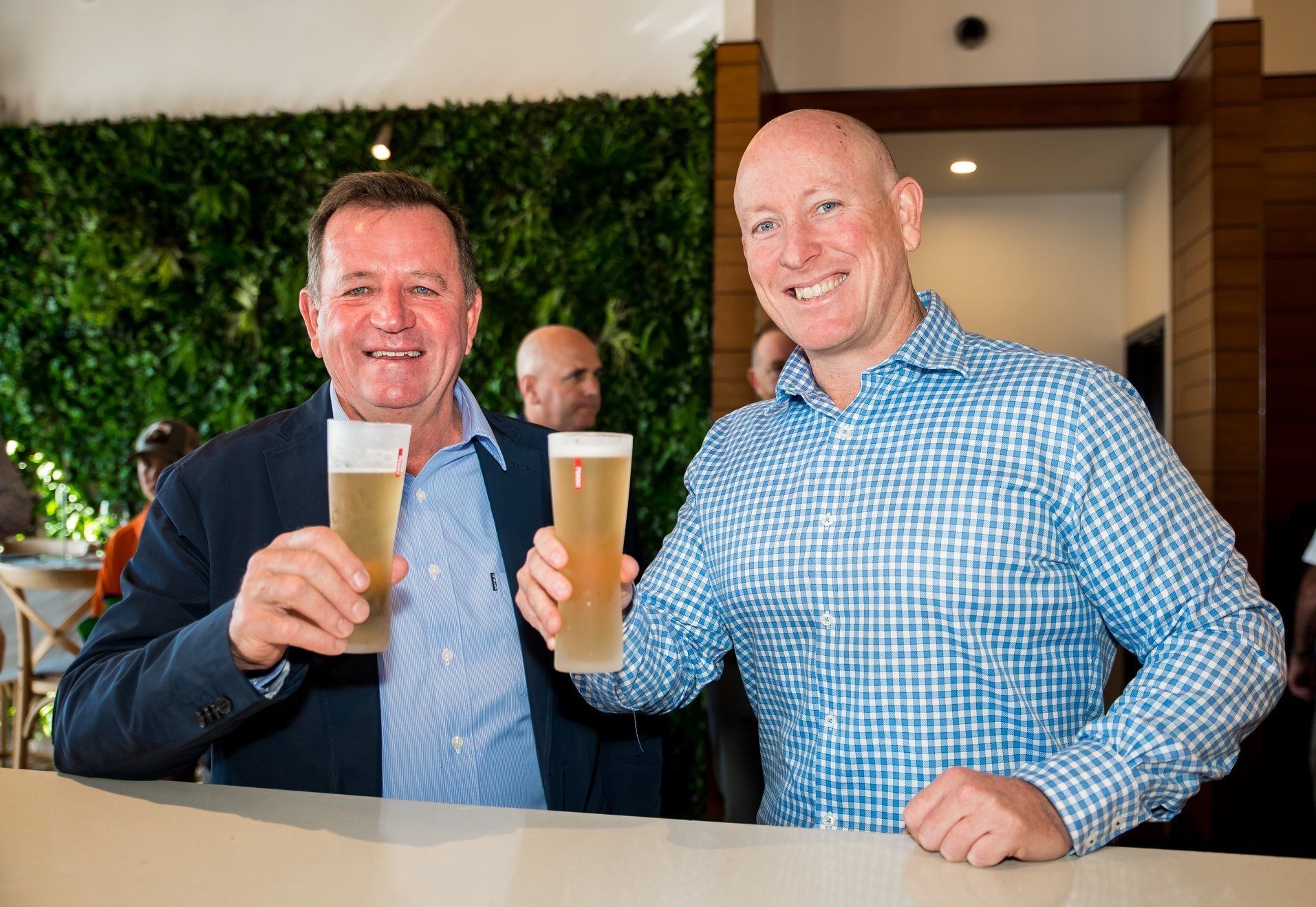 Two men are sitting at a bar holding glasses of beer.